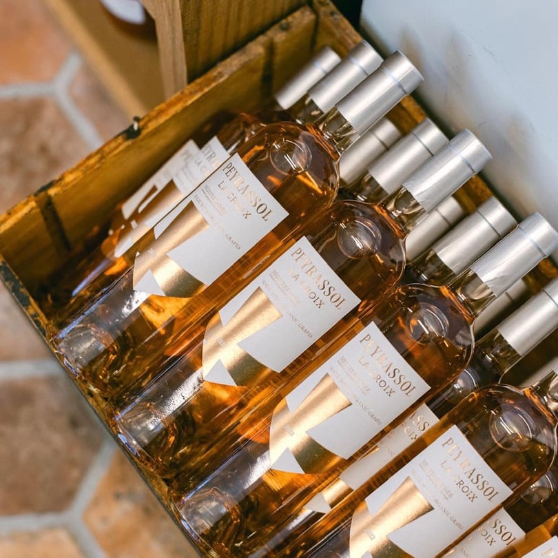 Rows of Peyrassol La Croix rosé wine bottles with gold labels in a wooden crate.