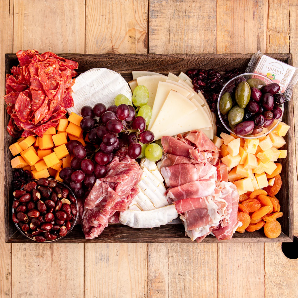 Overhead view of a large charcuterie board with various cheeses, meats, grapes, olives, and dried fruits.