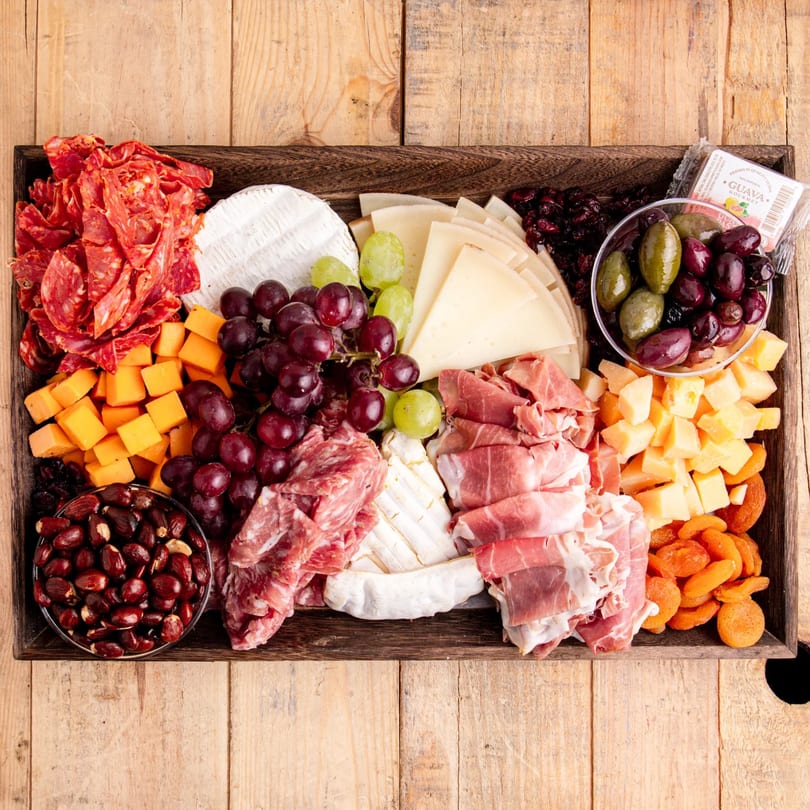 Overhead view of a large charcuterie board with various cheeses, meats, grapes, olives, and dried fruits.