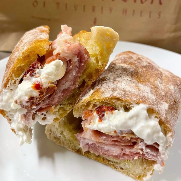 A deli sandwich from The Cheese Store of Beverly Hills, cut in half, revealing meat, cheese, and sun-dried tomatoes.