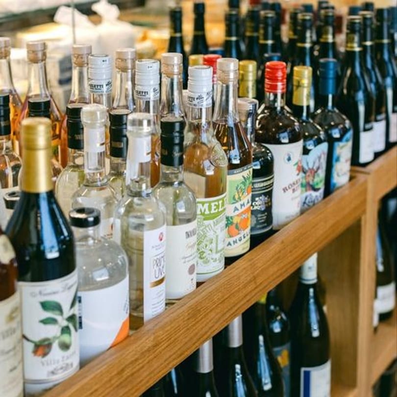 Rows of various bottled spirits and wines displayed on wooden shelves at The Cheese Store of Beverly Hills.