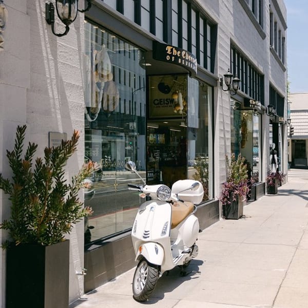 A white scooter parked on the sidewalk in front of The Cheese Store of Beverly Hills.