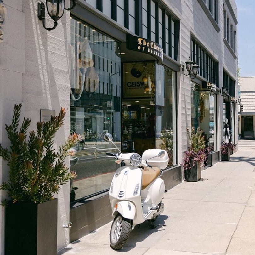A white scooter parked on the sidewalk in front of The Cheese Store of Beverly Hills.